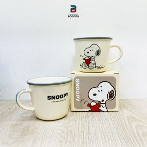 Taza de cerámica color crema con diseño de Snoopy sosteniendo una taza roja